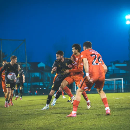 Na boisku piłkarskim zawodnicy walczą o piłkę w intensywnej akcji pod sztucznym oświetleniem.