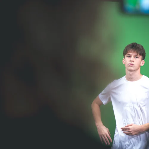 Młody mężczyzna w białej koszulce pozuje na tle zielonego ekranu.