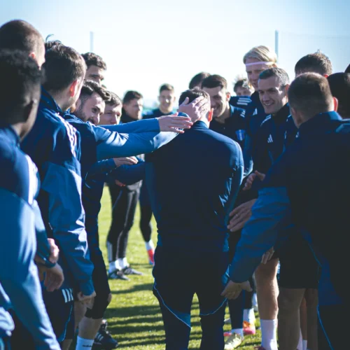 Grupa sportowców stoi w szeregach, witając jednego z kolegów, który przechodzi przez utworzoną przez nich bramkę.