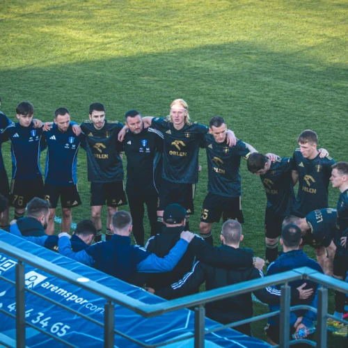 Zawodnicy drużyny piłkarskiej zbierają się w kręgu przed meczem, wspierając się nawzajem i przygotowując do rywalizacji.