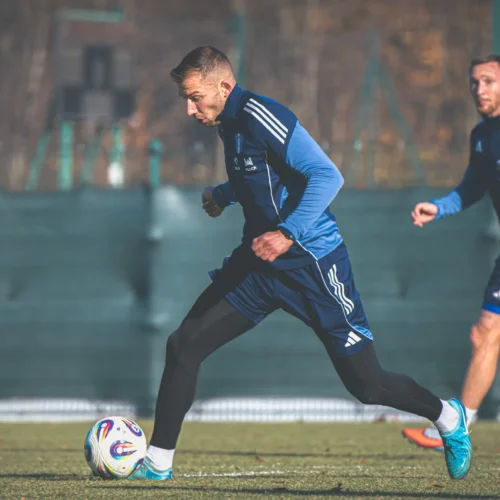 Na zdjęciu widać dwóch piłkarzy w niebieskich strojach, którzy biorą udział w treningu na boisku piłkarskim.