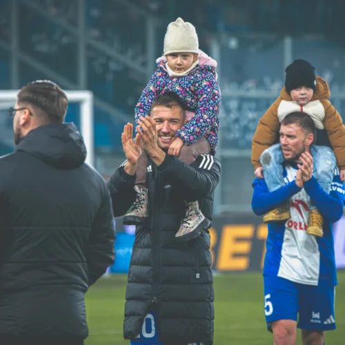 Na zdjęciu widać radosnych piłkarzy, którzy po meczu trzymają na ramionach dzieci, a atmosfera jest pełna entuzjazmu.