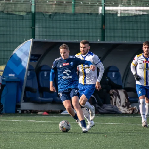 Na zdjęciu widać dwóch piłkarzy rywalizujących o piłkę na boisku, w dynamicznej akcji w trakcie meczu.