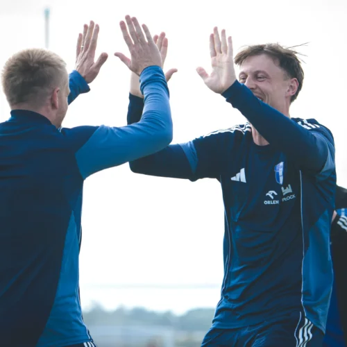 Dwaj piłkarze witają się radośnie na boisku, celebrując udany moment.