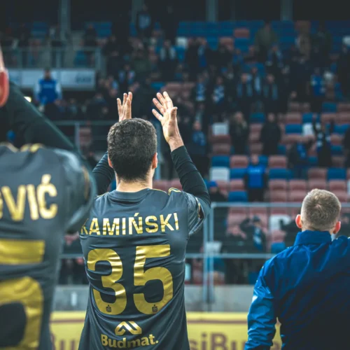 Na zdjęciu widać piłkarzy w czarnych strojach, którzy wiwatują w kierunku tłumu kibiców na trybunach.