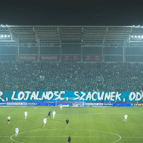 Na zdjęciu widać kibiców na stadionie, którzy prezentują transparent z napisem: „HONOR, LOJALNOŚĆ, SZACUNEK, ODWAGA”.