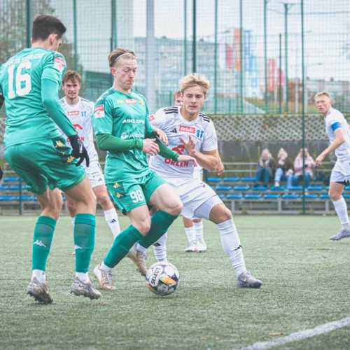 Na zdjęciu widoczni są piłkarze w trakcie intensywnej akcji na boisku, zbliżający się do piłki na sztucznej nawierzchni.