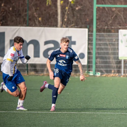 Na zdjęciu dwóch piłkarzy rywalizuje o piłkę na boisku sportowym.