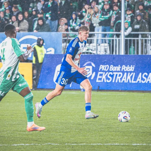 Na zdjęciu widać dwóch piłkarzy na boisku podczas meczu, w deszczową pogodę, w akcji w trakcie rozgrywki.