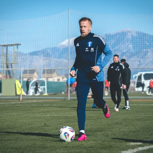 Na zdjęciu widać piłkarza podczas treningu na boisku, obok stoją innych zawodników oraz różnorodne elementy treningowe w tle.