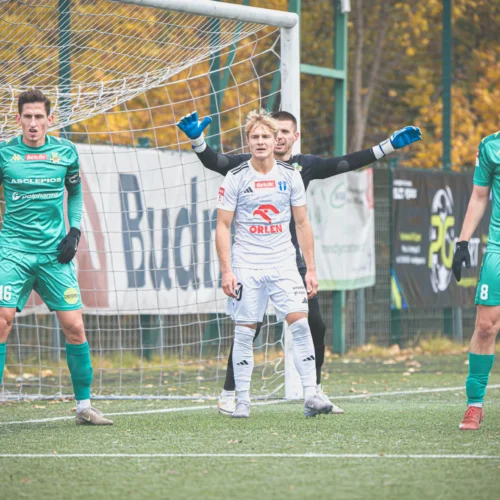 Na zdjęciu widoczni są futboliści przygotowujący się do rzutu karnego, z bramkarzem w zielonym stroju i zawodnikami w białych oraz zielonych koszulkach.