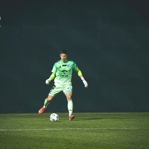 Na zdjęciu widoczny jest bramkarz w zielonym stroju, który przygotowuje się do obrony piłki na boisku.