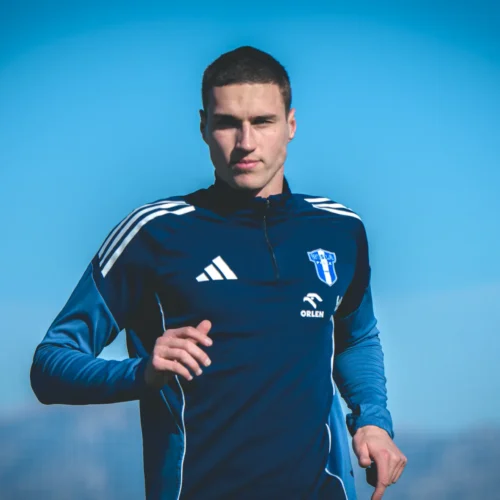 Mężczyzna w niebieskiej odzieży sportowej biegnie na boisku w jasny, słoneczny dzień.