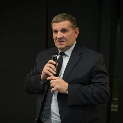 Mężczyzna w garniturze trzyma mikrofon i przemawia podczas wystąpienia.