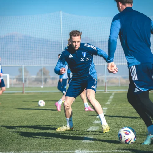 Na zdjęciu widać grupę piłkarzy trenujących na boisku, wykonujących dynamiczne ruchy podczas ćwiczeń z piłką.