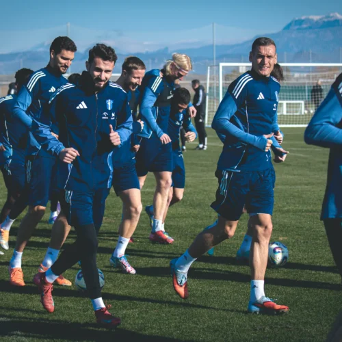 Grupa piłkarzy trenuje na boisku w słoneczny dzień.