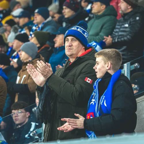 Na zdjęciu widać kibiców w tłumie, którzy gromko klaskają i wspierają swoją drużynę na stadionie.