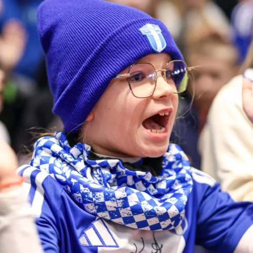 Na zdjęciu widać radosną dziewczynkę w niebieskiej czapce i szaliku, entuzjastycznie reagującą na wydarzenie.