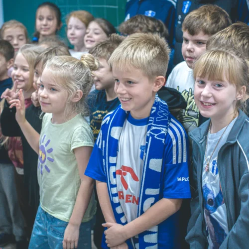 Na zdjęciu widać grupę dzieci, które uśmiechają się i pozują do zdjęcia, część z nich trzyma ręce w geście zwycięstwa.