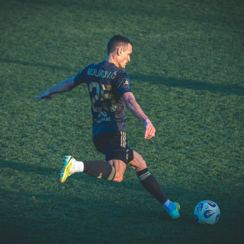 Piłkarz w trakcie wykonywania strzału na zielonym boisku.