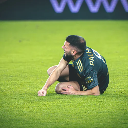 Piłkarz leży na zielonej murawie, trzymając się za nogę z wyrazem bólu na twarzy.