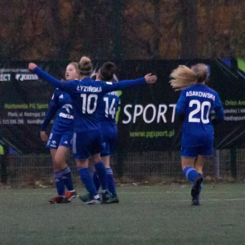 Na zdjęciu widoczne są radosne zawodniczki drużyny piłkarskiej celebrujące strzeloną bramkę na boisku.