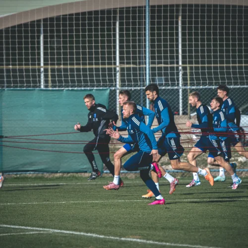 Zespół sportowy trenuje na boisku, biegając w równym szyku z użyciem elastycznych taśm.