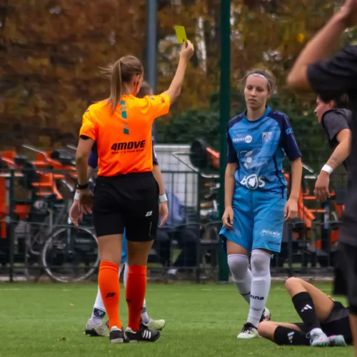 Sędzia piłkarski pokazuje żółtą kartkę zawodniczce podczas meczu na boisku.