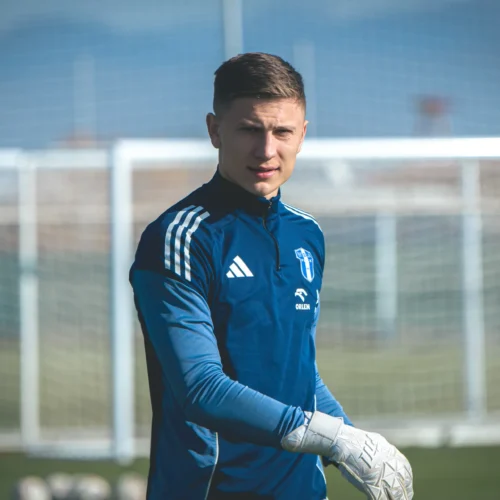 Na zdjęciu młody piłkarz w niebieskim stroju bramkarskim, przygotowujący się do treningu na boisku.