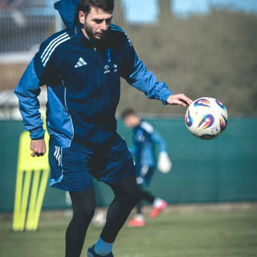 Na zdjęciu widać sportowca trenującego piłkę nożną na boisku.