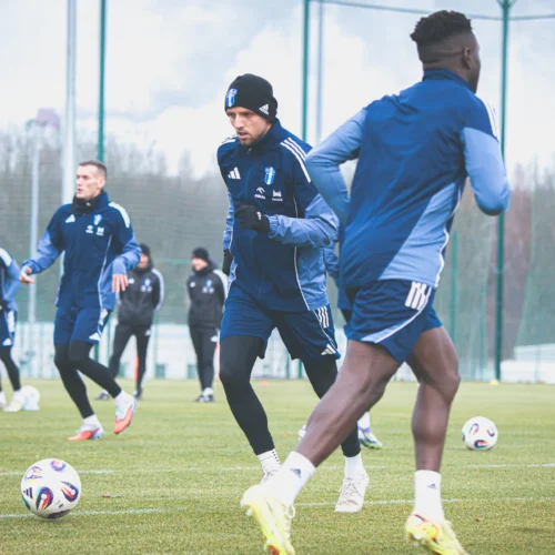 Na zdjęciu widoczni są piłkarze trenujący na boisku, wykonujący ćwiczenia w niebieskich strojach sportowych.