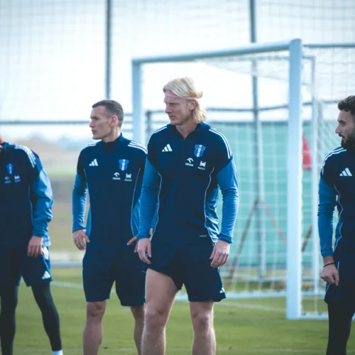 Na zdjęciu widoczni są czterej zawodnicy w niebieskich strojach treningowych podczas treningu na boisku piłkarskim.