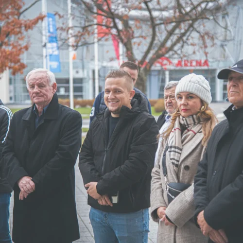 Grupa osób w formalnych ubraniach stoi w radosnej atmosferze na tle nowoczesnego budynku.