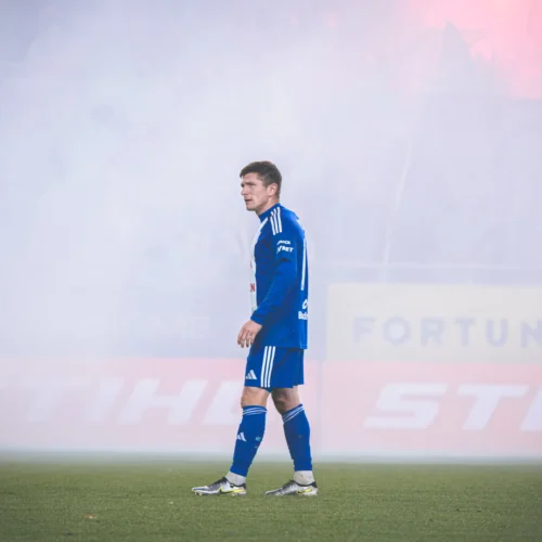Na zdjęciu widoczny jest piłkarz w niebieskim stroju, który stoi na boisku otoczony gęstą mgłą.