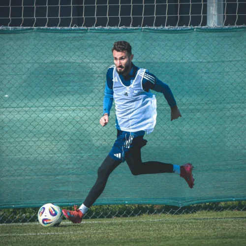 Mężczyzna w stroju sportowym biega za piłką na boisku treningowym.