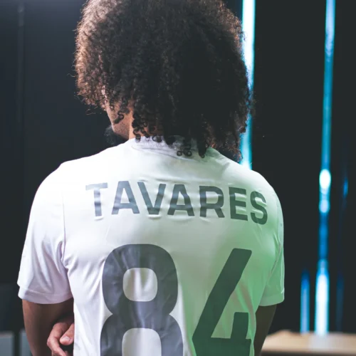 Na zdjęciu widać osobę z kręconymi włosami, która stoi tyłem i nosi biały t-shirt z nazwiskiem "TAVARES" oraz numerem "84".