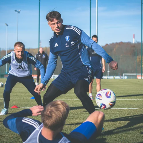 Na zdjęciu widać kilku piłkarzy podczas treningu na boisku, skoncentrowanych na grze z piłką.