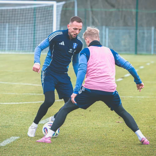 Dwóch piłkarzy trenuje na boisku, wykonując dynamiczne ruchy z piłką.