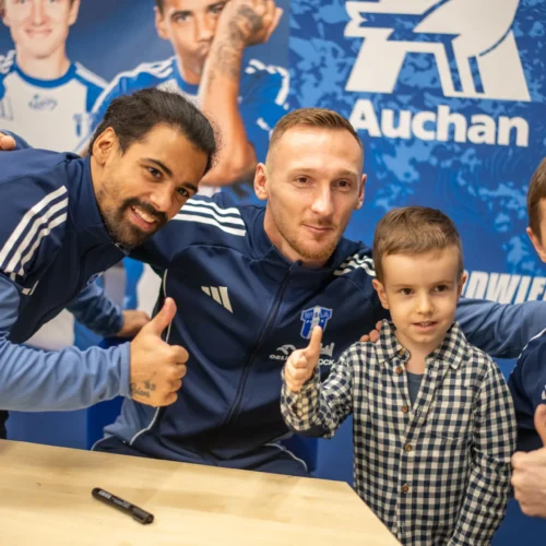 Na zdjęciu trzech sportowców pozuje z uśmiechniętym małym chłopcem, wszyscy pokazują kciuki w górę.