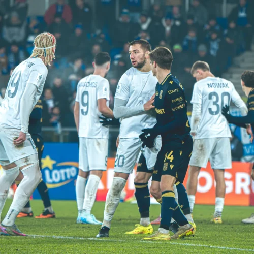 Na zdjęciu zawodnicy dwóch drużyn piłkarskich dyskutują na boisku podczas meczu.