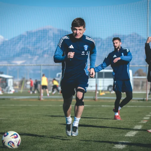 Na zdjęciu widać piłkarzy podczas treningu na boisku, z górami w tle.