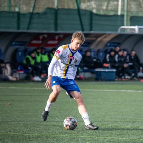 Na zdjęciu młody zawodnik gra w piłkę nożną na boisku, przygotowując się do kopnięcia piłki, podczas treningu lub meczu.