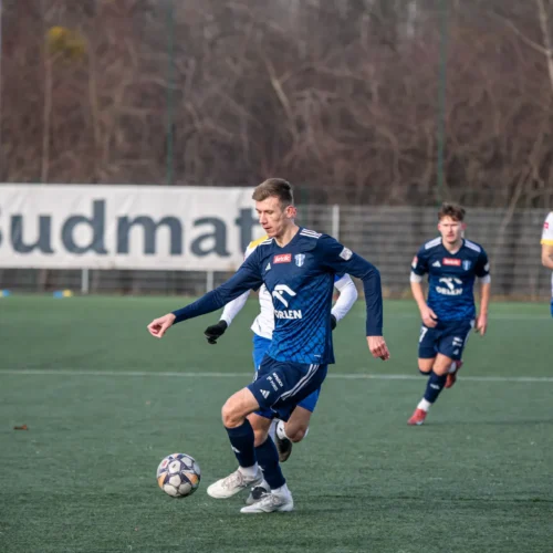 Na zdjęciu widać futbolistę w niebieskim stroju, który kontroluje piłkę na boisku podczas meczu piłkarskiego.