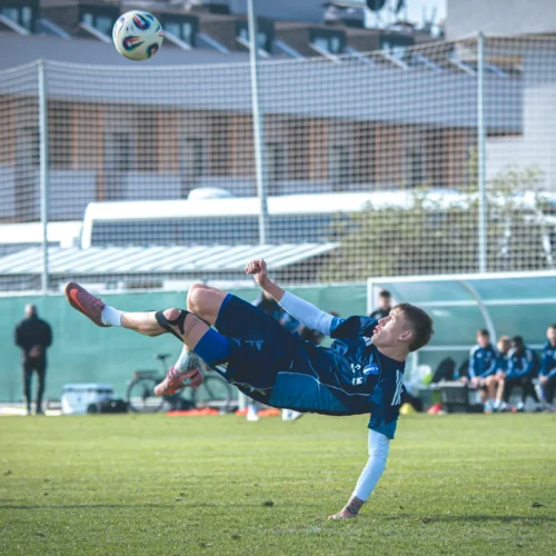 Na zdjęciu widać młodego piłkarza wykonującego akrobatyczny strzał w trakcie treningu na boisku sportowym.