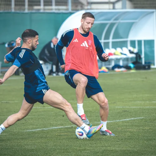 Dwaj piłkarze intensywnie trenują na boisku, próbując przejąć piłkę.